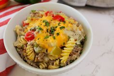 a white bowl filled with pasta and meat covered in cheese on top of a red and white table cloth