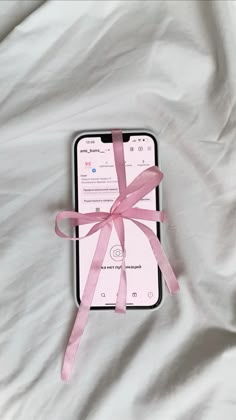 an iphone with a pink ribbon tied around it on top of a white bed sheet