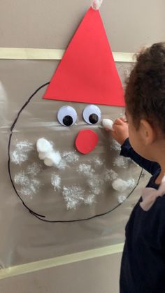 a young child painting a snowman face on a sheet of clear paper with googly eyes