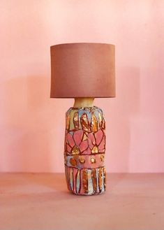 a lamp that is on a table with a pink wall behind it and a brown shade