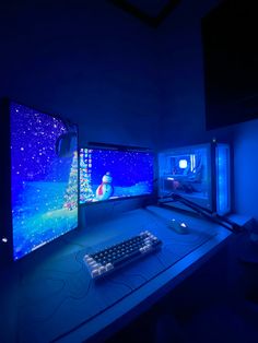 two computer monitors sitting next to each other on top of a blue desk in a dark room