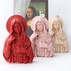 three candles in the shape of virgin mary and jesus with an image of christ behind them