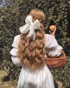 a woman with long red hair holding an apple in her hand and wearing a white dress