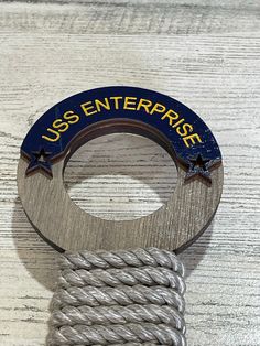 a close up of a metal object on a wooden surface with ropes and an inscription that reads usss enterprise