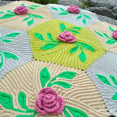 a crocheted umbrella with flowers and leaves on the ground next to some rocks