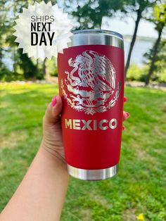 a person holding up a red cup with the words mexico on it in front of some grass