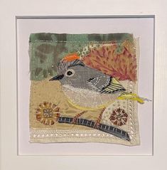 a bird is sitting on top of a piece of fabric in a white framed frame