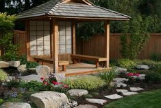 a wooden gazebo surrounded by rocks and flowers