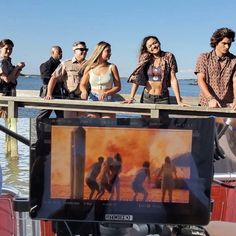 a group of people standing on top of a boat next to the ocean in front of a screen