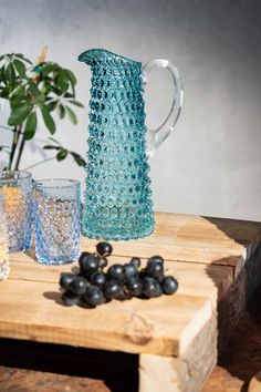 a blue glass pitcher sitting on top of a wooden table next to glasses and grapes