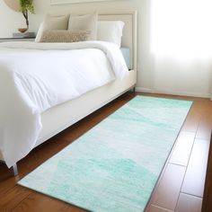 a white bed sitting next to a window on top of a hard wood floor