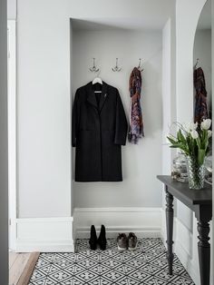 a coat and shoes are sitting on the floor in front of a wall with two coats hanging from hooks