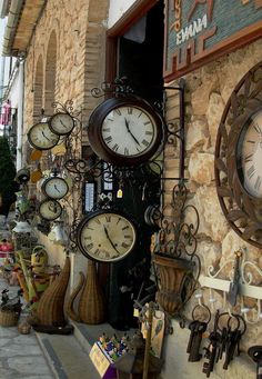 several clocks are hanging on the side of a building in front of a storefront