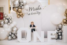 a little boy sitting on top of a white chair in front of balloons and letters