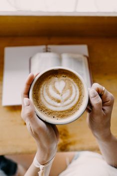 a person holding a cup of coffee with a book on the table in front of them