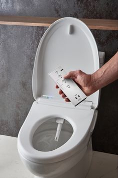 a person using an electronic device to flush a toilet