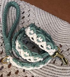 a crocheted white and green leash with brass hardware on top of a rug