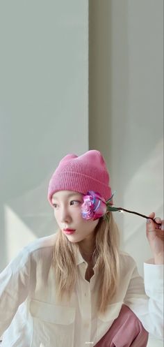 a young woman wearing a pink hat and holding a flower in one hand while sitting down