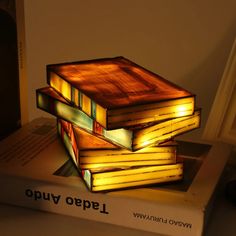 a stack of books sitting on top of each other next to a lamp that is lit up