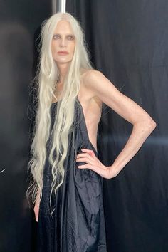 a woman with long white hair standing in front of a black backdrop