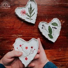 two heart shaped plates with flowers painted on them, one being held in the other hand