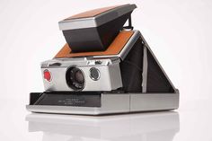 an old fashioned polaroid camera sitting on top of a white surface with its lens up