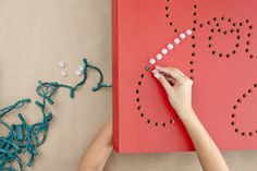 a woman is making a string art project on a red board with beads and scissors