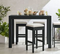 three stools and a table with plants on it in front of a white wall