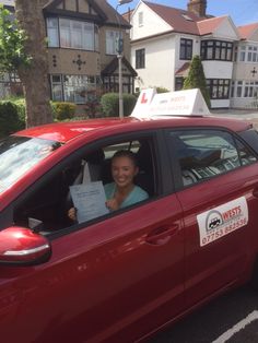 a woman sitting in the driver's seat of a red car holding up a sign