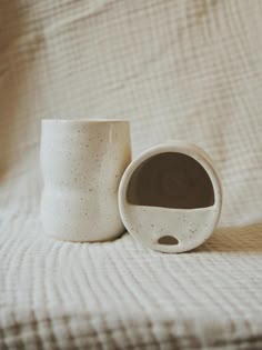 two white cups sitting on top of a bed next to each other in front of a blanket