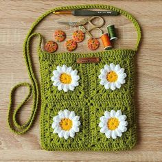 a green crocheted purse with white and yellow flowers on the front, two orange buttons in the middle