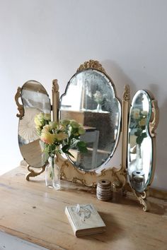 a table topped with mirrors and vases filled with flowers next to a book on top of a wooden table