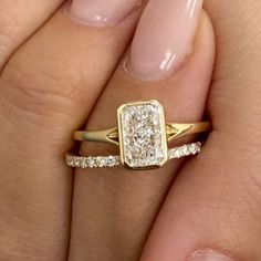 a woman's hand holding a gold ring with two diamonds on the middle and one diamond in the middle