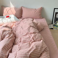 an unmade bed with pink comforter and pillows on it next to a framed photograph