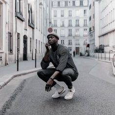 a man squatting down while talking on a cell phone in the middle of an empty street