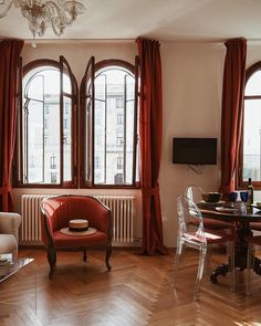 a living room filled with furniture next to two large windows covered in red drapes