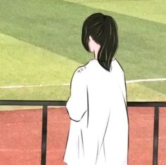 a girl standing in front of a fence looking at a soccer field with grass on it