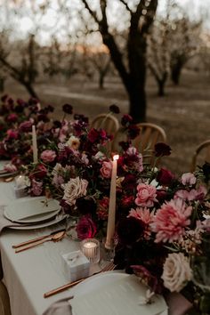 a long table with flowers and candles on it is set for an outdoor dinner party