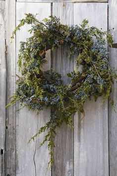 a wreath is hanging on the side of a wooden door with blue berries and greenery