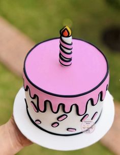 a pink and black cake with a candle on top is held up by someone's hand