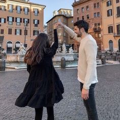 a man and woman are standing in front of some buildings with their arms up to each other