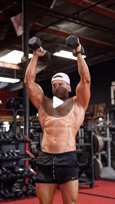 a shirtless man lifting two dumbbells in a gym