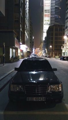 a black car parked on the side of a street at night in front of tall buildings