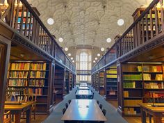 the library is full of books and many tables with benches on them are lined up in rows