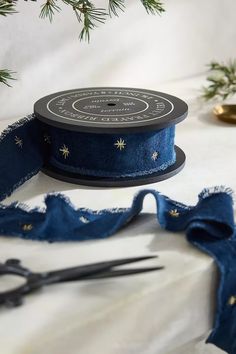 a spool of blue ribbon next to some scissors on a table with pine branches