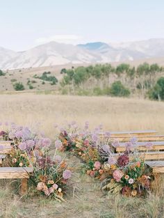 an outdoor ceremony with wooden benches and flowers on the back ground, in front of mountains