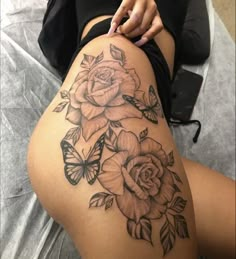 a woman's thigh with roses and butterflies tattoo on her leg, sitting on a bed