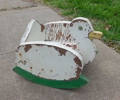 an old wooden duck shaped toy sitting on the side of a road next to grass