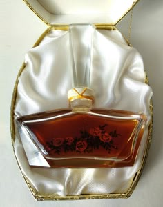 an empty bottle in a gold box with white satin around the edges and roses on it