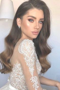 a woman with long hair sitting on top of a table wearing a white dress and earrings